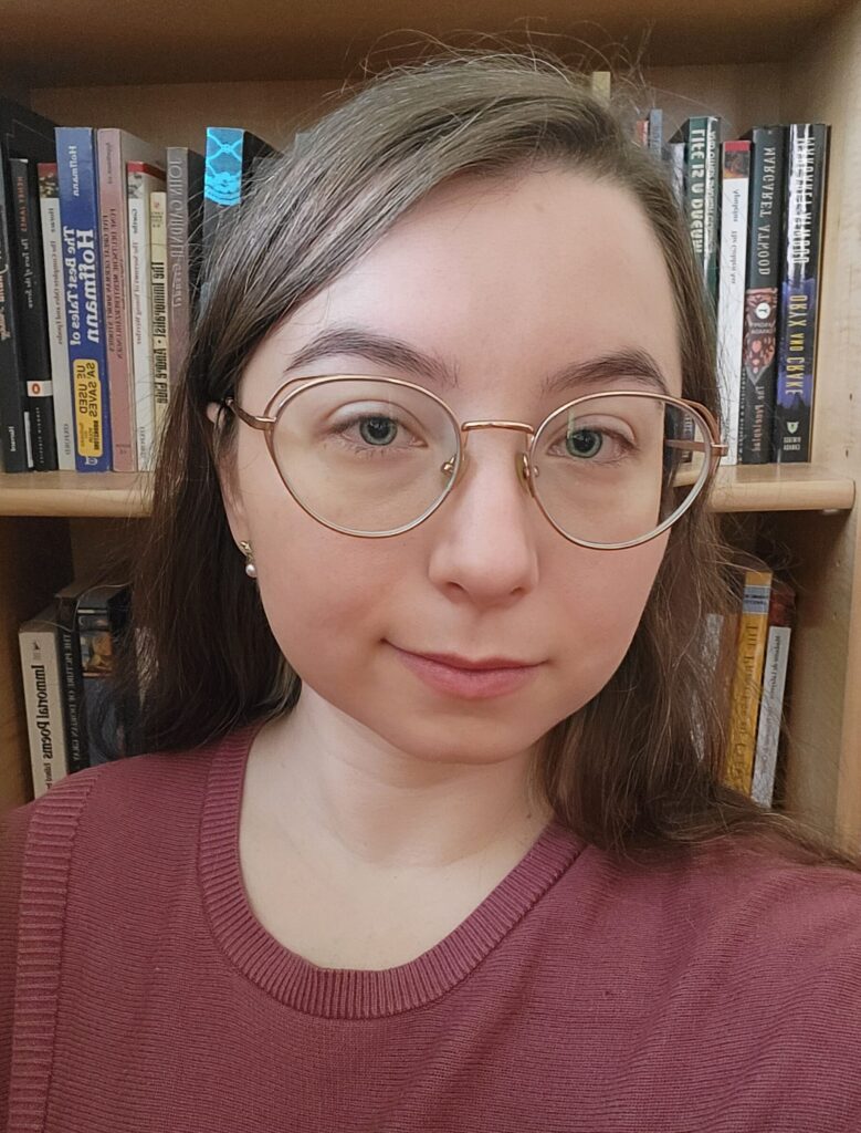 Photo of Helen Hey wearing a mauve sweater in front of a bookshelf